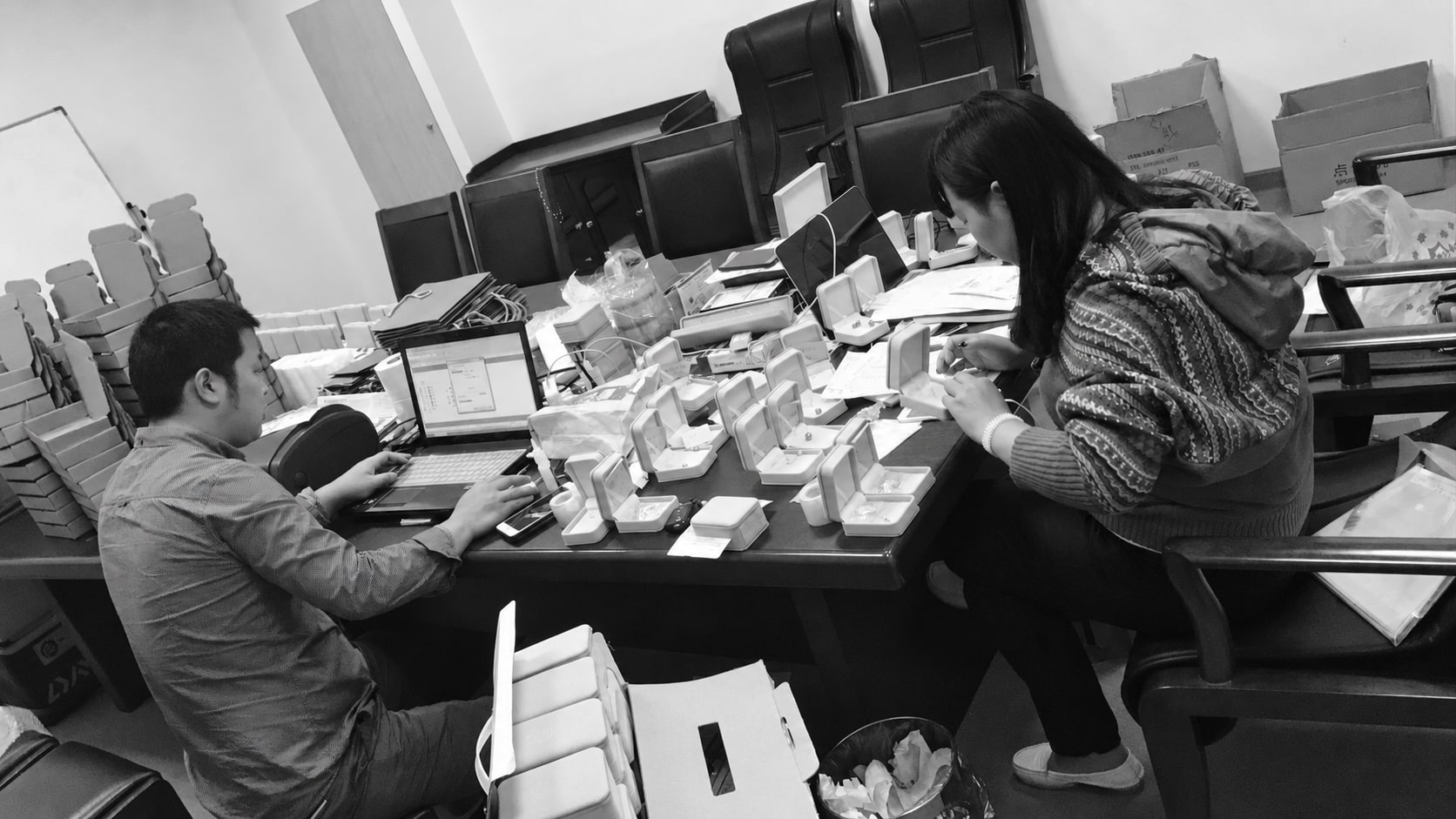 Early jewellery preparation: a team member works at a laptop while another arranges jewellery boxes.